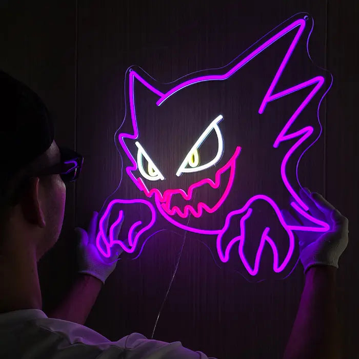 Geist Neon LED Schild wird an die Wand gehalten, lila Kontur und pinkes Grinsen leuchten im dunklen Raum