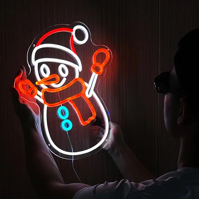 Schneemann Neon LED Schild leuchtend vor einer Holzwand, komplettes Motiv mit Schal und Fäustlingen
