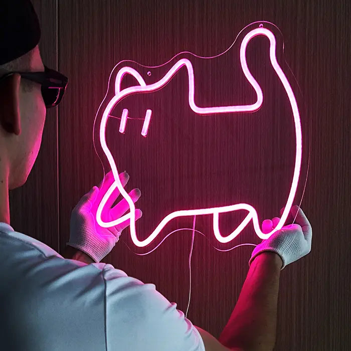Pinke Katze Neon LED Schild wird mit Handschuhen an einer dunklen Holzwand montiert, das Motiv leuchtet rosa