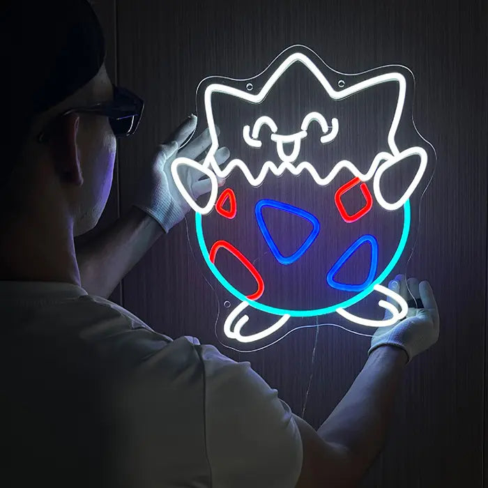 Eierschalen-Figur Neon LED Schild wird mit Schutzhandschuhen an der Wand ausgerichtet, Kontur leuchtet weiß und hellblau