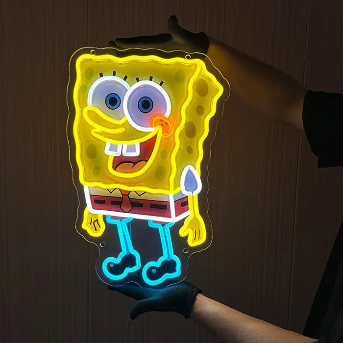 Schwammfigur Neon LED Schild frontal vor der Wand, leuchtende Augen, roter Gürtel und türkise Beine