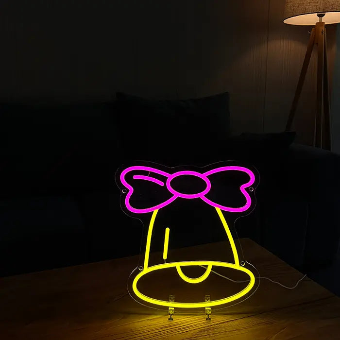 Little Bell Neon LED Sign standing on a wooden table with a sofa and floor lamp behind it in a dark room