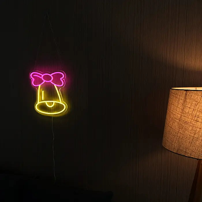 Little Bell Neon LED Sign hanging on a dark wooden wall with a floor lamp glowing warmly beside it