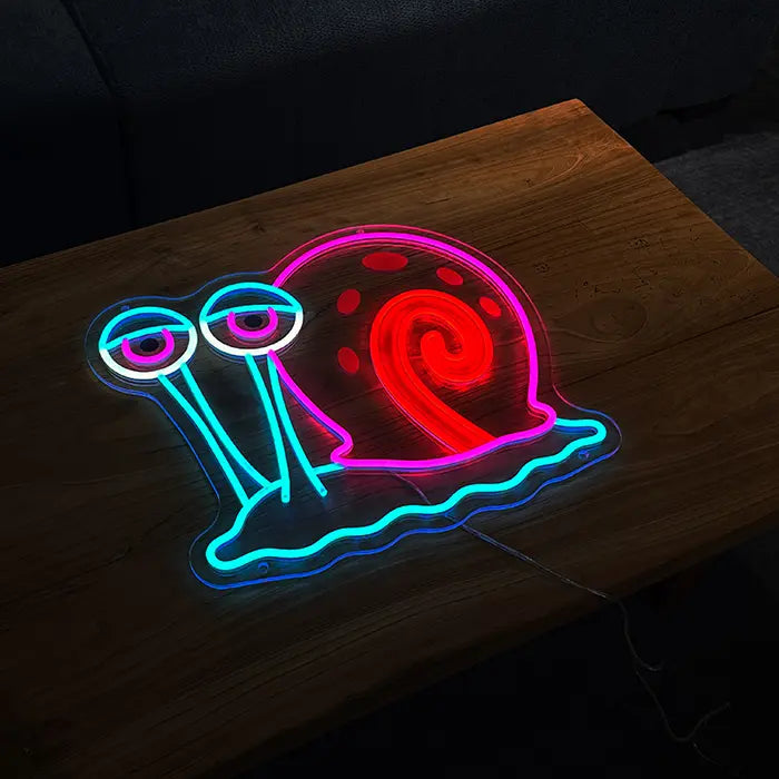 Gary the Snail Neon LED Sign standing on a wooden table with a sofa behind it in a dark room