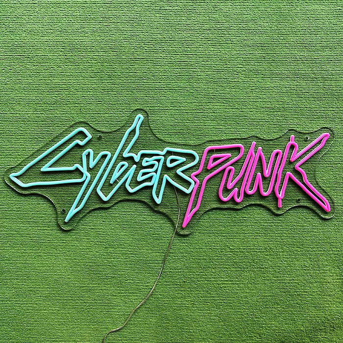 CYBERPUNK Neon LED Sign switched off on a green surface, the complete lettering visible