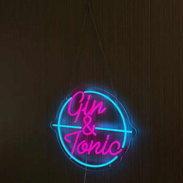 Gin & Tonic Neon LED Sign hung on chains in front of a dark wooden wall, pink and turquoise glowing