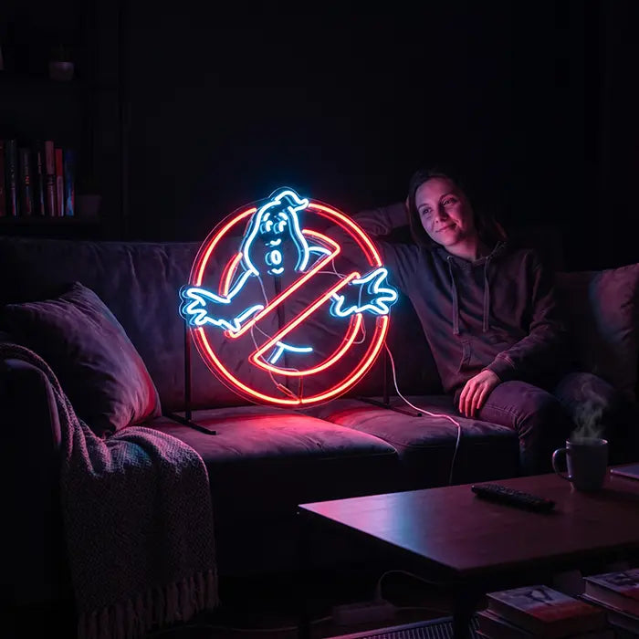 Ghostbusters Logo Neon LED Schild steht auf Standfüßen auf einem Sofa und leuchtet rot-weiß in den dunklen Raum