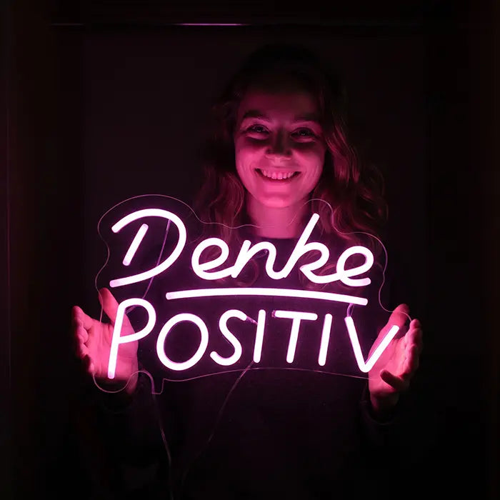 Denke Positiv Neon LED Schild leuchtet rosa, in beiden Händen vor dunklem Hintergrund gehalten