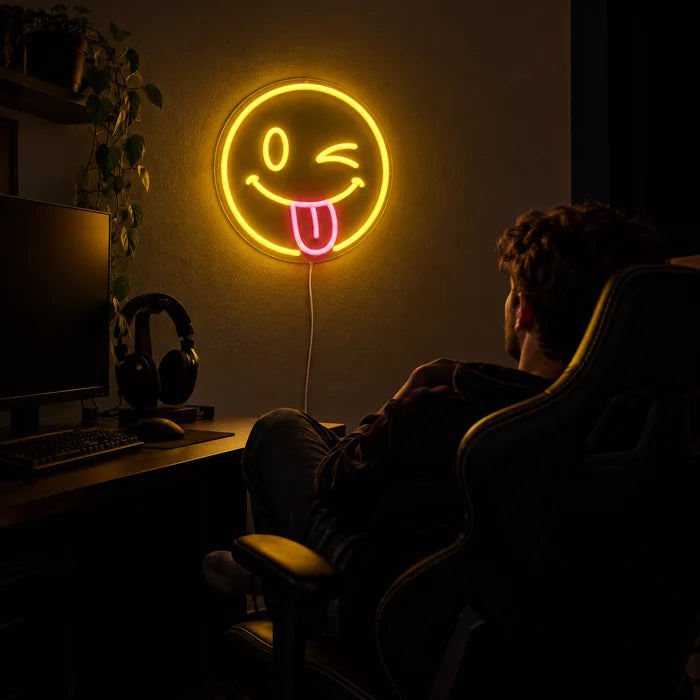 Cheeky Smiley Neon LED Sign above a gaming desk, a gamer in a gaming chair in front of it