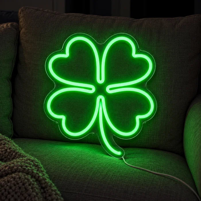 Neon LED-skilt Lykkekløver på en koselig sofa mellom puter og pledd