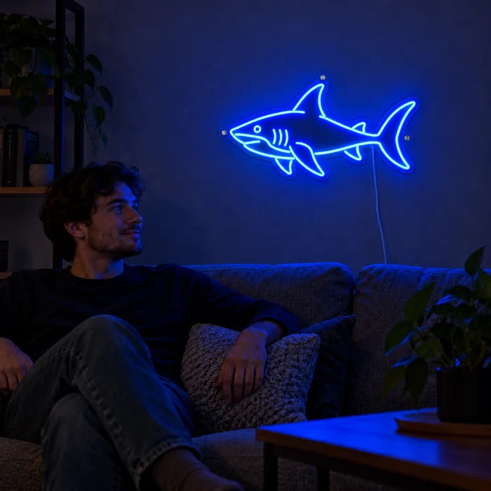 لافتة نيون LED سمكة القرش، على جدار غرفة المعيشة، وأمامها شخص مسترخٍ على الأريكة