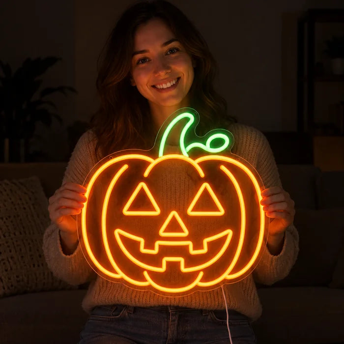 Halloweengræskar neon LED skilt i hænderne på en smilende kvinde mod mørk baggrund