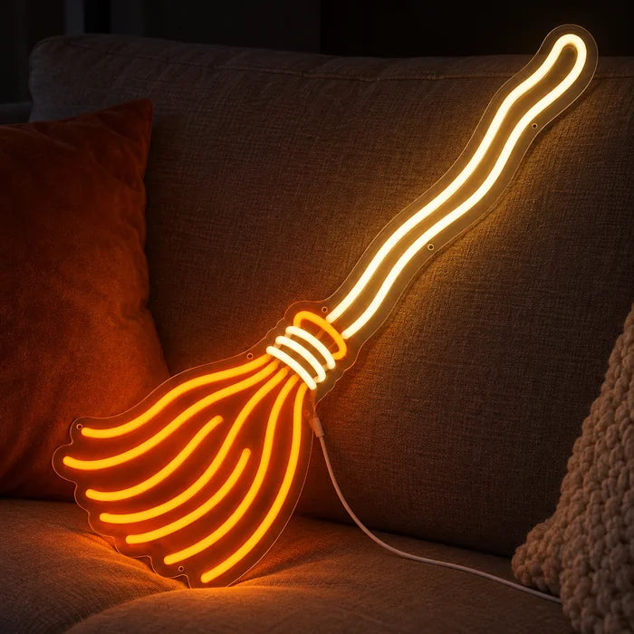 Noidan luuta neon LED -kyltti kodikkaalla sohvalla tyynyjen ja huovan välissä