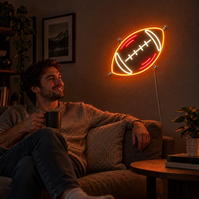 Rugbypallo neon LED -kyltti olohuoneen seinällä, edessä henkilö rentoutuu sohvalla