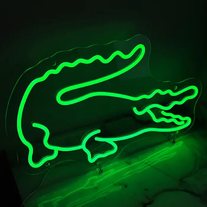 Krokodil Neon LED Schild leuchtet grün auf einer Marmorfläche stehend, Reflexion im hellen Stein sichtbar