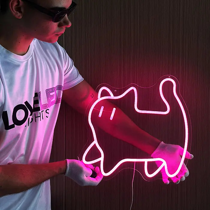 Pinke Katze Neon LED Schild wird vor einer Holzwand gehalten, die rosa leuchtende Katzenkontur auf klarem Acryl