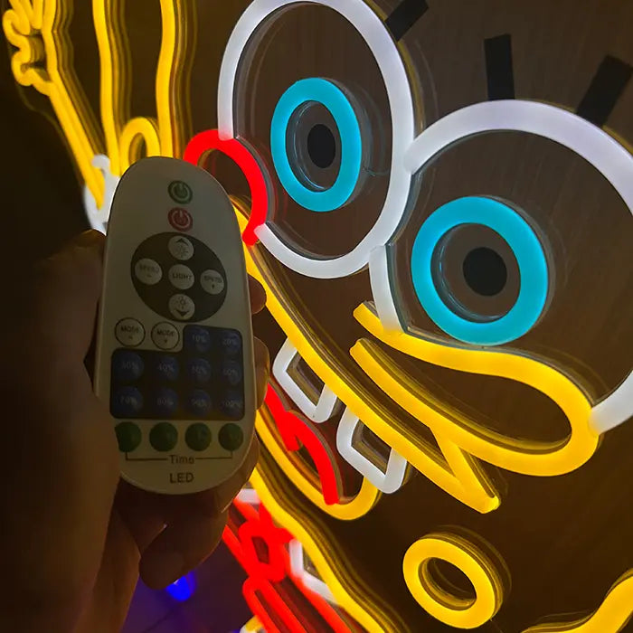 Schwammfigur Neon LED Schild aus der Nähe, davor die Dimmer-Fernbedienung vor den blau leuchtenden Augen