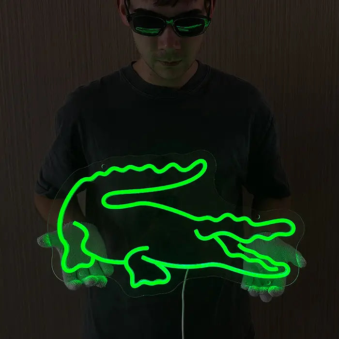 Krokodil Neon LED Schild leuchtet grün vor einer dunklen Holzwand, gehalten in Höhe der Wandmontage