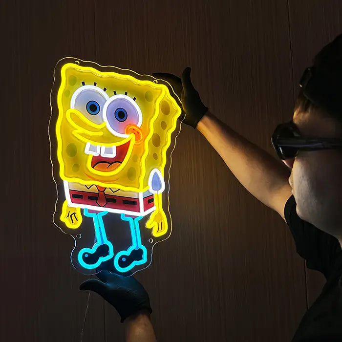 Schwammfigur Neon LED Schild wird an der Wand ausgerichtet, gelbe Kontur und blaue Beine leuchten kräftig