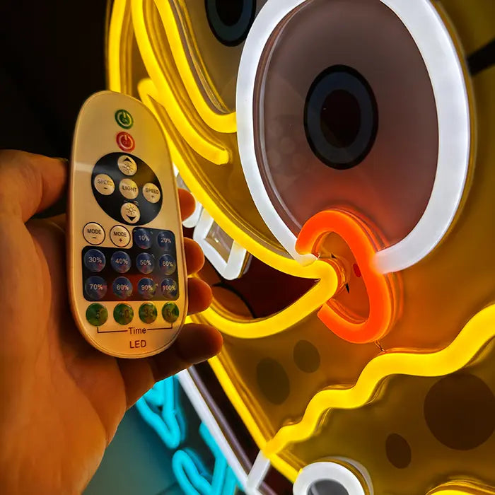 Schwammfigur Neon LED Schild aus der Nähe mit Fernbedienung davor, weißer Augenring und oranger Nasenbogen