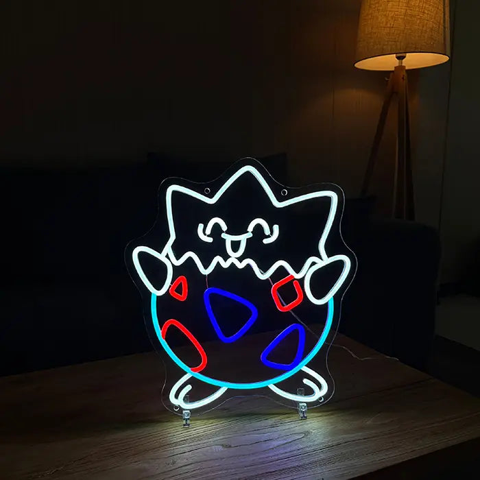 Pokémon Togepi Neon LED Sign standing on a wooden table with a warm floor lamp behind it
