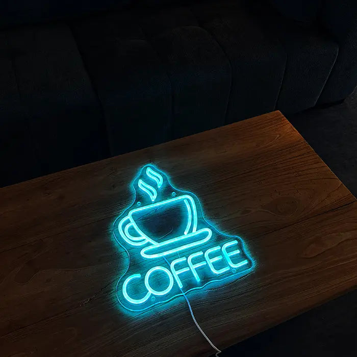 Coffee Cup Neon LED Sign lying on a wooden table, cup and lettering glowing ice blue