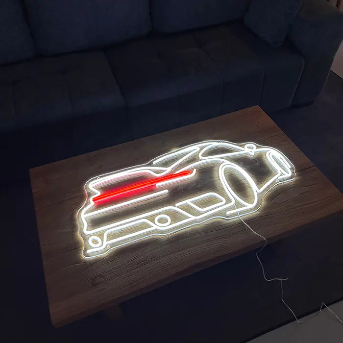 GT Sports Car Neon LED Sign lying on a wooden table in front of a sofa, glowing white and red
