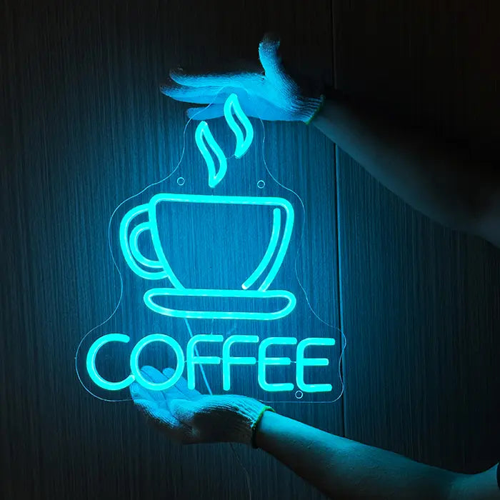 Coffee Cup Neon LED Sign being held against a dark wooden wall with gloves