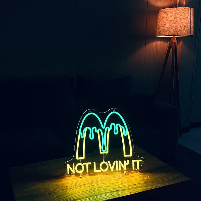 McDonald's Not Lovin' It Neon LED Sign on a wooden table in a dark living room, next to it a floor lamp