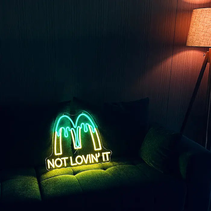 McDonald's Not Lovin' It Neon LED Sign set up on a dark sofa, next to it a floor lamp