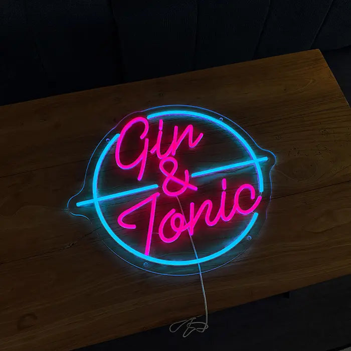 Gin & Tonic Neon LED Sign lying on a wooden table, lettering in pink, circle in turquoise