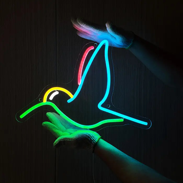 Hummingbird Bird Neon LED Sign being held against a dark wooden wall with gloves