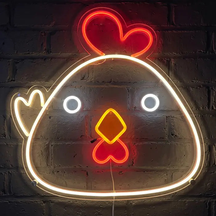 Little Chicken neon LED sign as outlines: warm-white glowing outline of a round chicken with a red comb, white eyes and yellow beak against a brick wall
