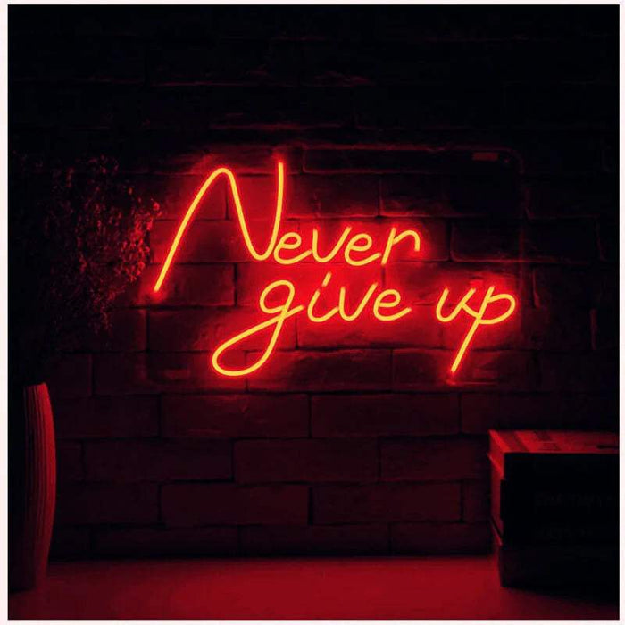 Never Give Up Neon LED Sign in red, two lines of handwritten lettering on a dark brick wall
