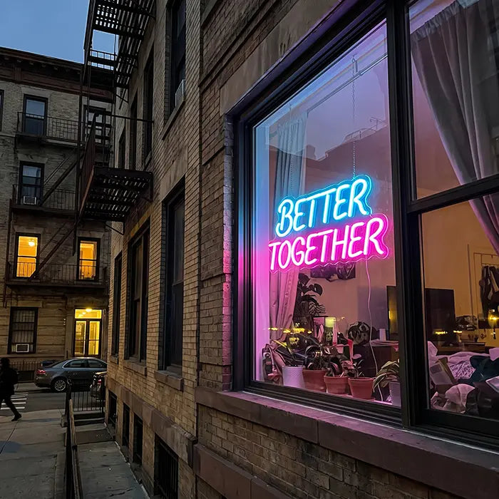 Better Together Neon LED Sign in blue-pink in the window of a brick house, seen from the street