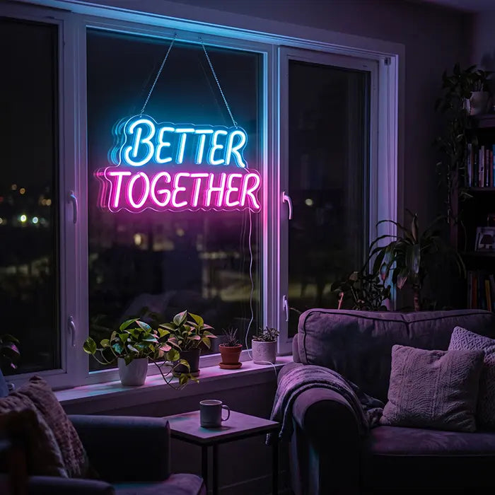 Better Together Neon LED Sign in blue-pink in a window with plants, a sofa in front