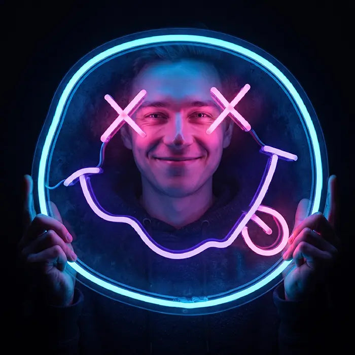 Smiley Neon LED Schild wird vor das Gesicht gehalten, blau-pinkes Leuchten im dunklen Raum