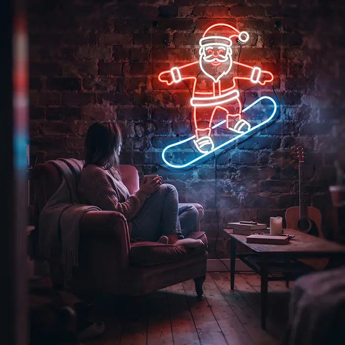 Snowboarding Santa Neon LED Sign on the wall above a woman in an armchair with a mug, a coffee table beside