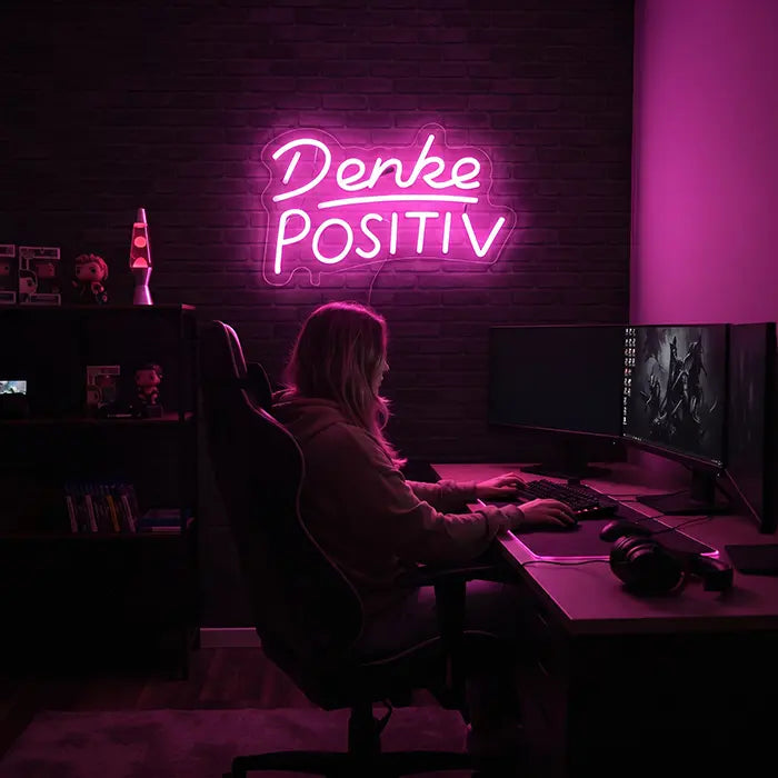Denke Positiv Neon LED Schild als rosa Blickfang an der Backsteinwand hinter einem Gaming-Schreibtisch