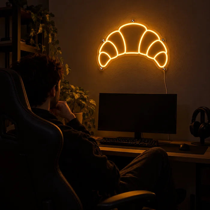 Butter Croissant Neon LED Sign above a gaming desk, a gamer in a gaming chair in front of it