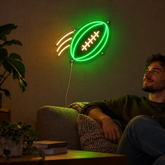 Flyvende football neon LED skilt på stuevæggen, foran slapper en person af på sofaen