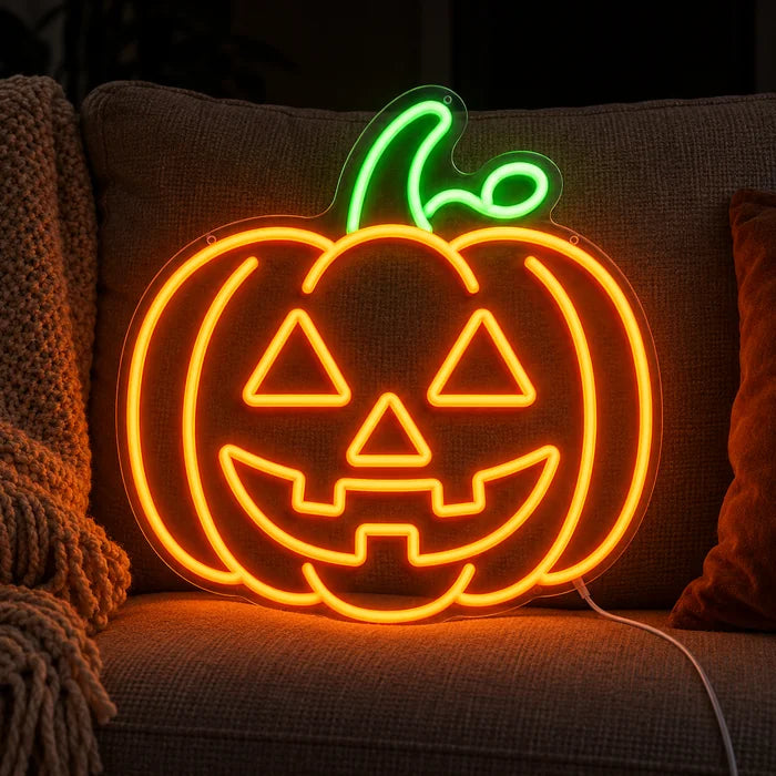 Halloweengræskar neon LED skilt på en hyggelig sofa mellem puder og tæppe
