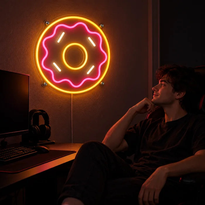 שלט ניאון LED דונאט ורוד מעל שולחן הגיימינג, לפניו שחקן בכיסא גיימינג