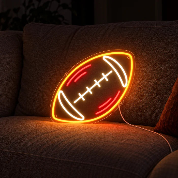 Rugbybold neon LED skilt på en hyggelig sofa mellem puder og tæppe