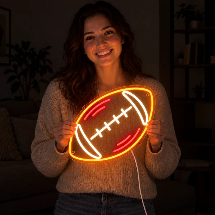 Rugbybold neon LED skilt i hænderne på en smilende kvinde mod mørk baggrund